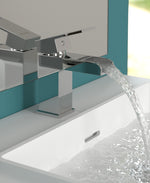 A contemporary silver mono basin faucet with water flowing from the tap, installed on a white basin with a chrome finish.
